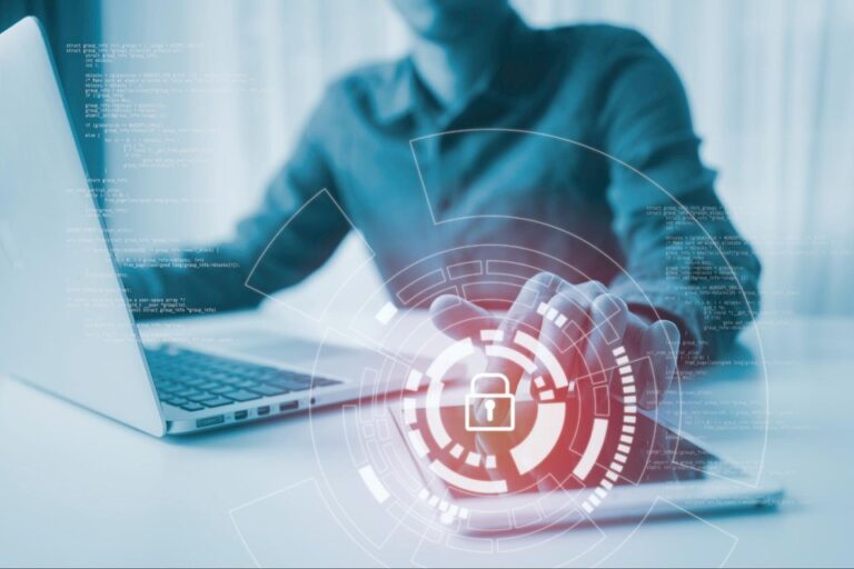 A cybersecurity professional using a laptop and tablet with a symbol in the foreground.