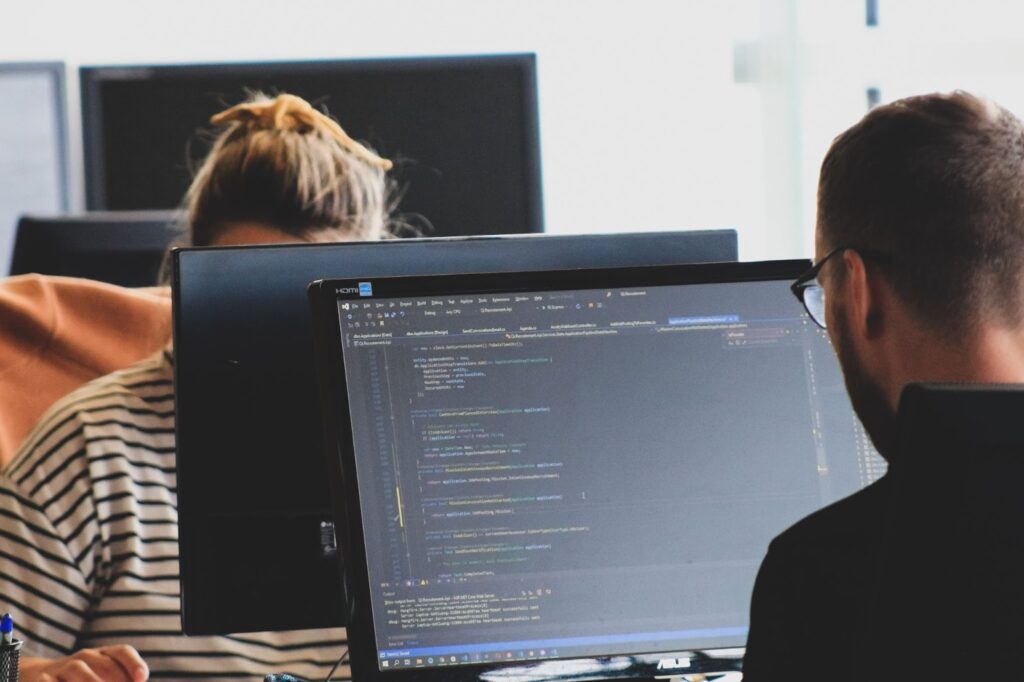 A Man and a Woman Sit Facing Each Other While Working on Two Separate Computers.