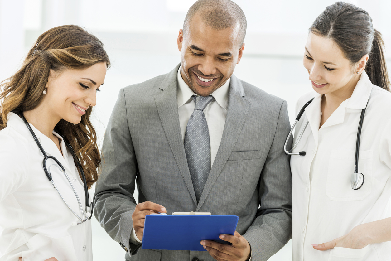 Hospital Administrator Talking With Two Doctors About Items on a List.