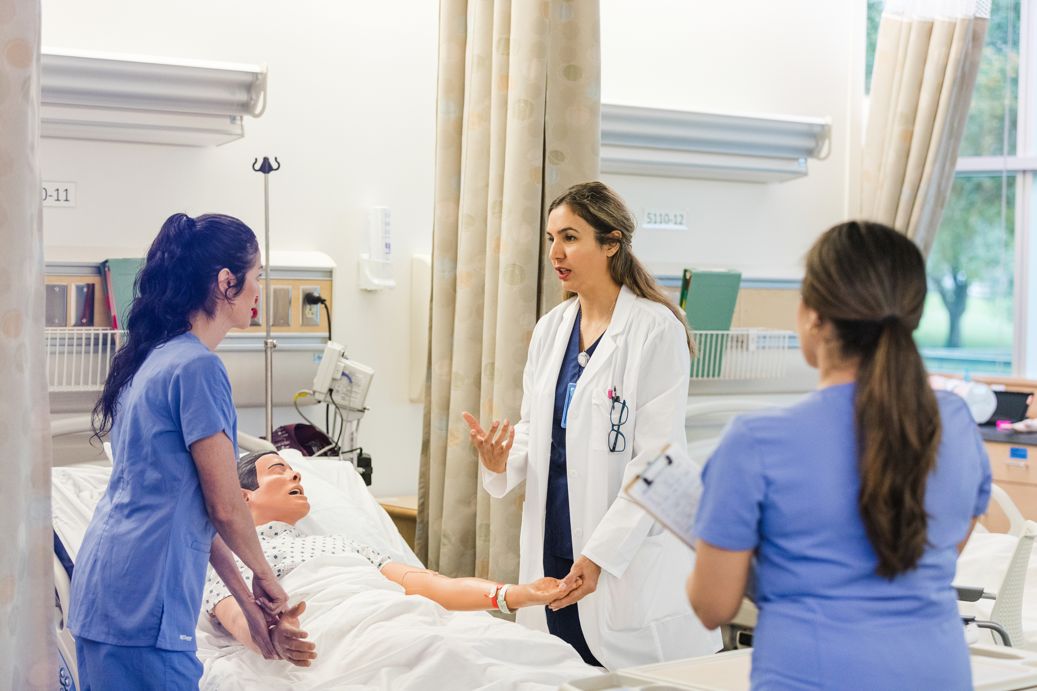 Nursing students listen to a professor demonstrating a procedure on a manikin.
