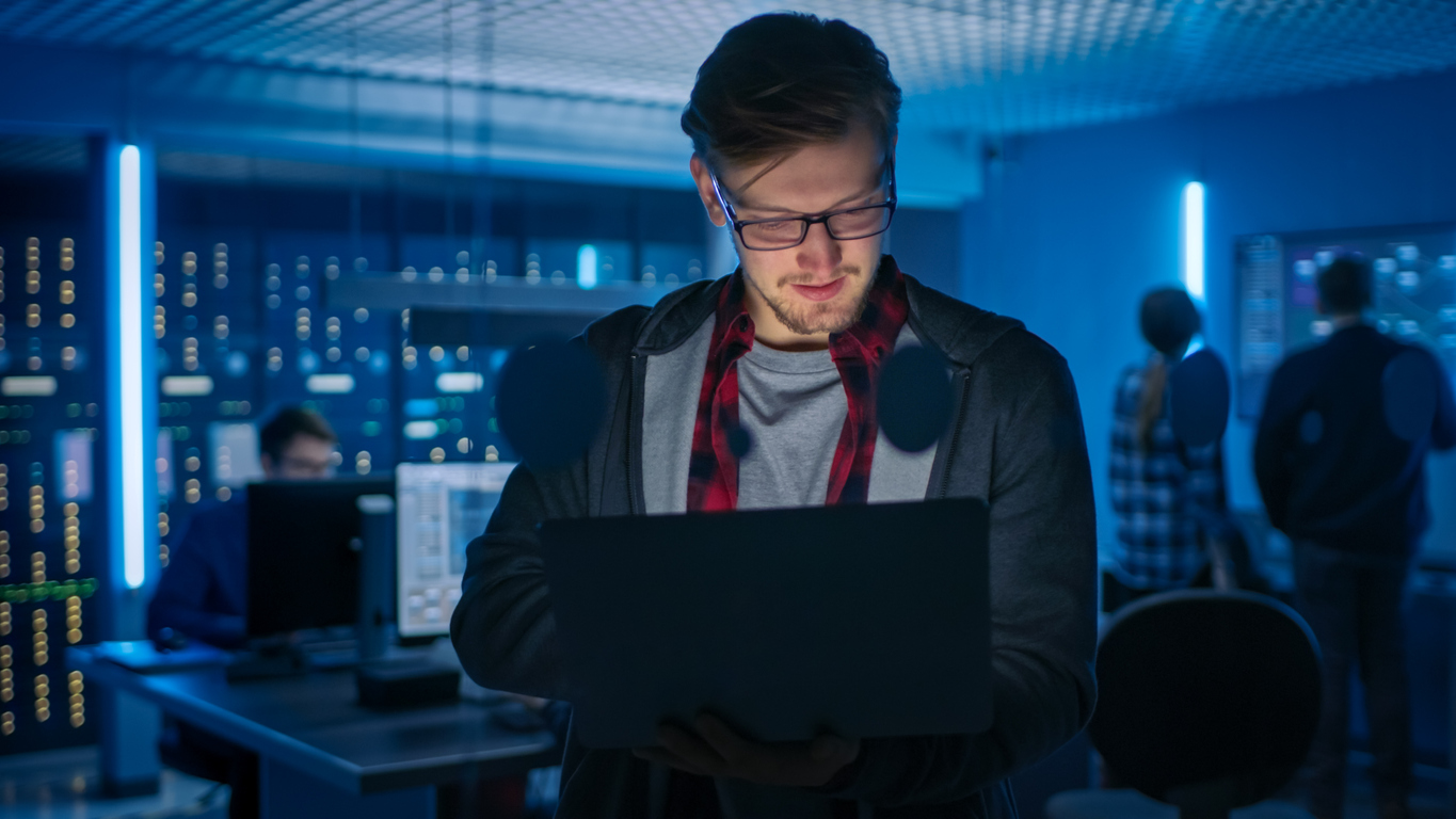 A Cyber Threat Analyst Works on a Laptop in a Server Room.