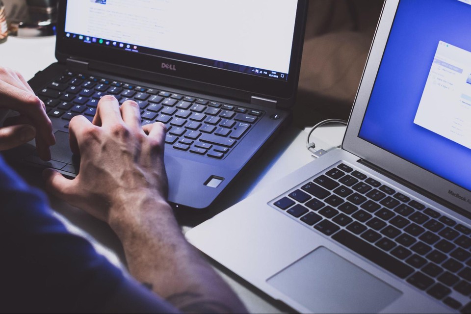 A man sits with two open laptops while working on one.