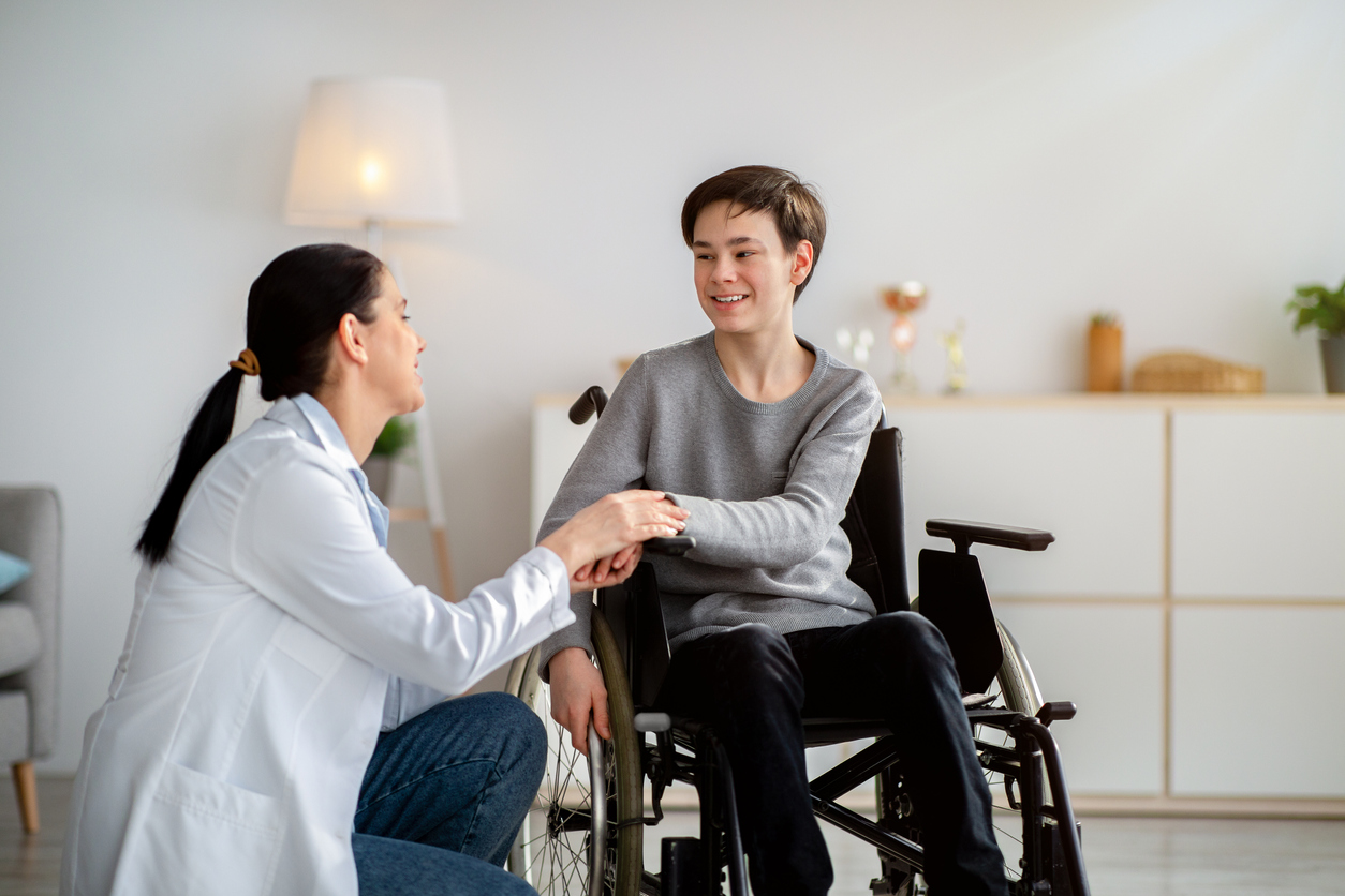 A Nurse Kneeling and Talking With a Teenage Patient in a Wheelchair.