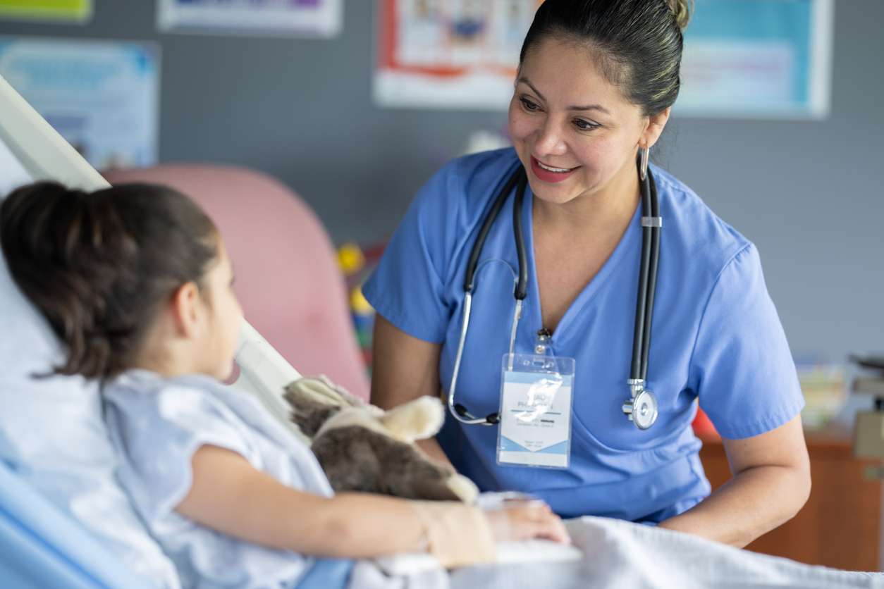 A Nurse Wearing Scrubs Visits a Young Patient in a Hospital Bed..jpg