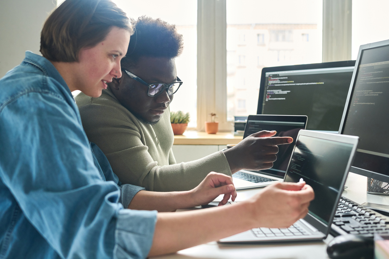 Two Cybersecurity Professionals Review Code on Laptops.