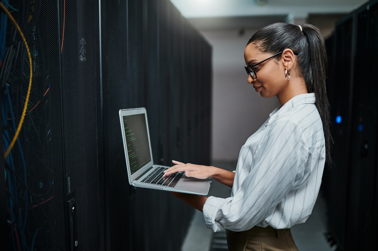 A Cybersecurity Professional Works on a Laptop in a Server Room.