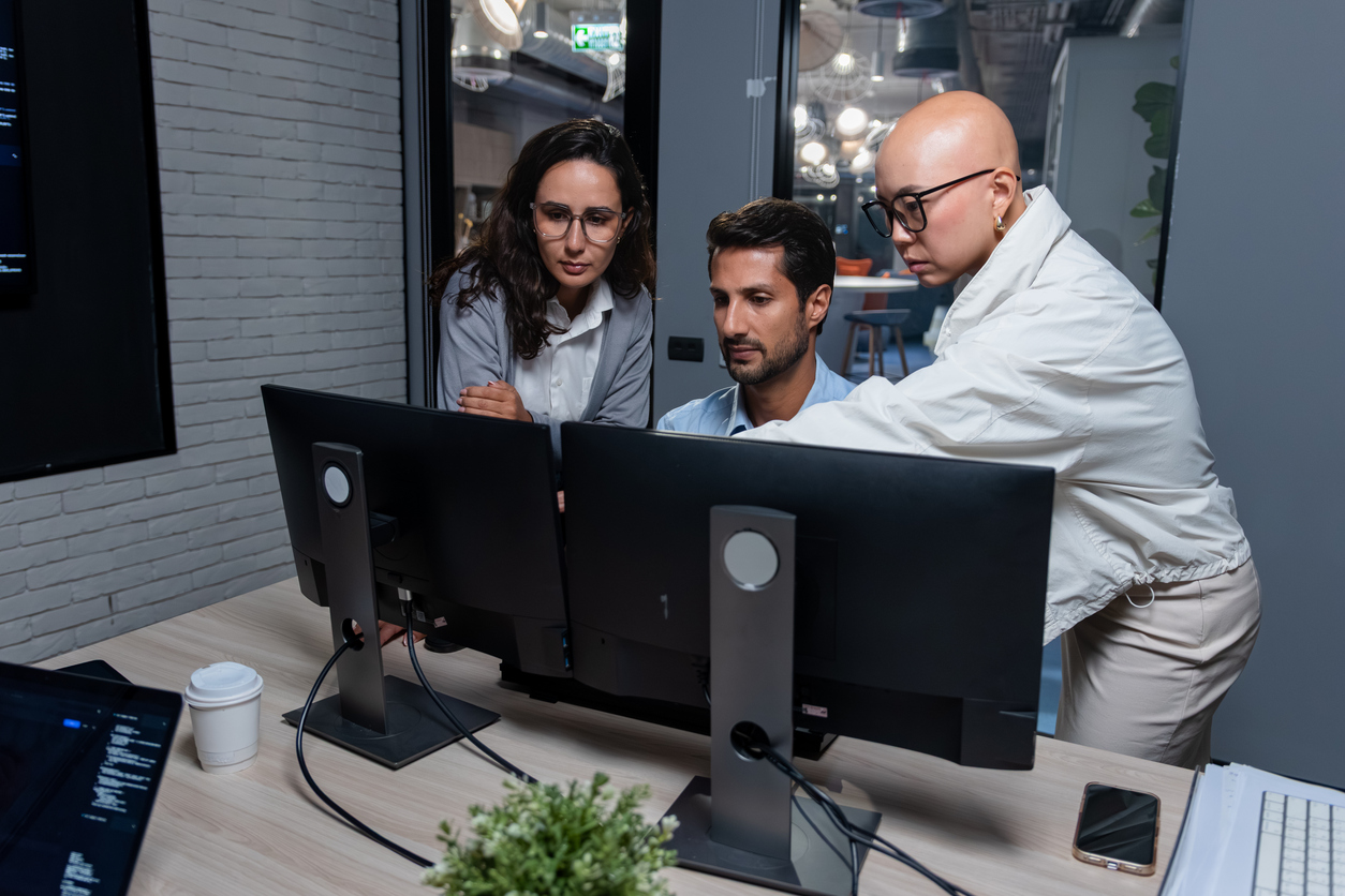 Three cybersecurity professionals collaborate at a computer workstation.