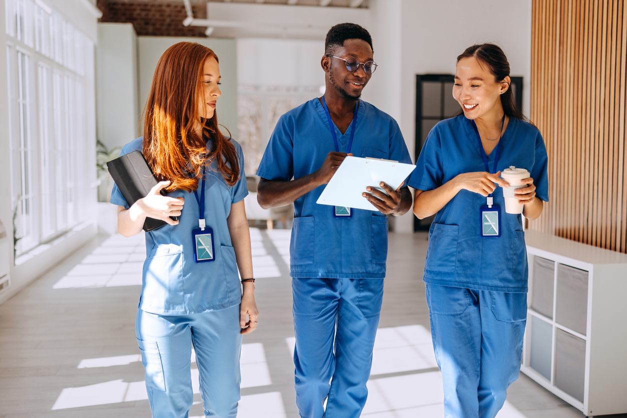 Three Nurses Wearing Scrubs Walk Down a Hospital Corridor.