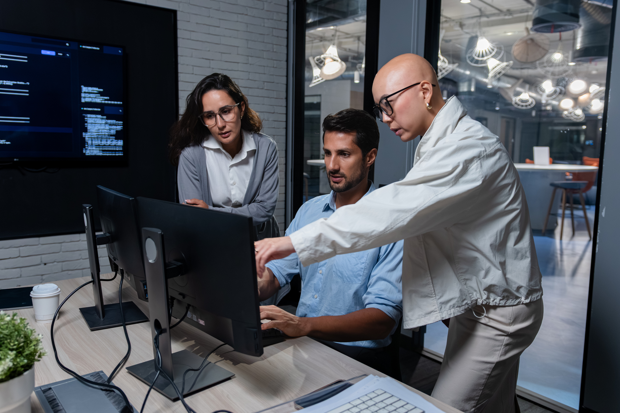 Three members of a cybersecurity team review code on a monitor.