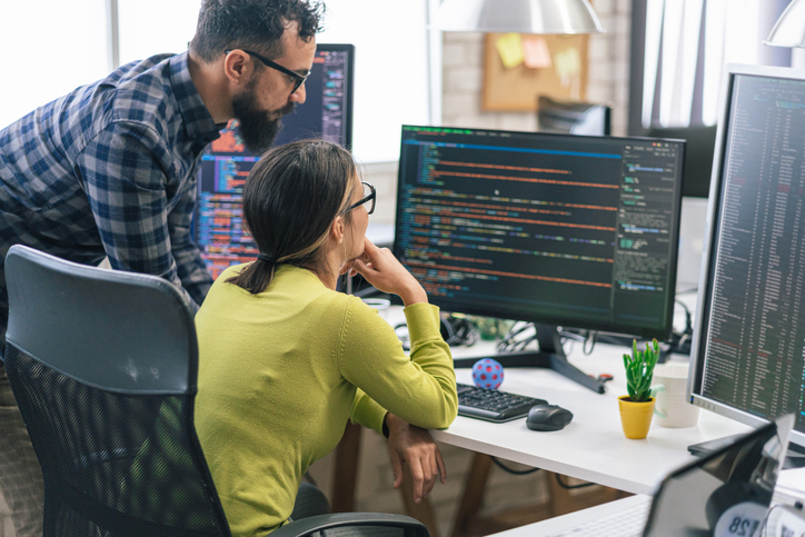 Two cybersecurity professionals review code on a monitor.