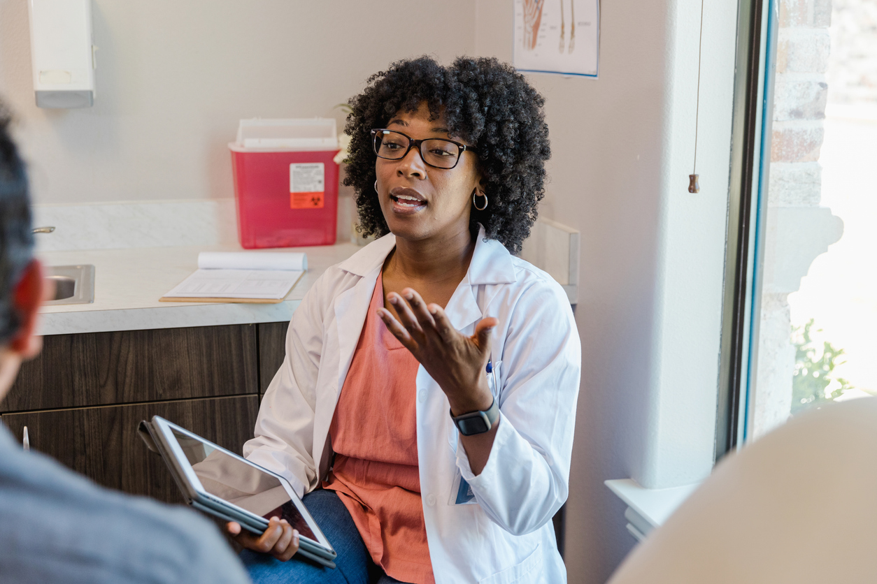 A nurse practitioner sits and talks to a patient in a medical office.