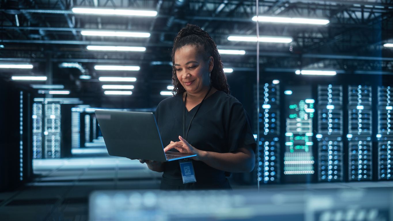 A cybersecurity professional holding a laptop works in a data center.