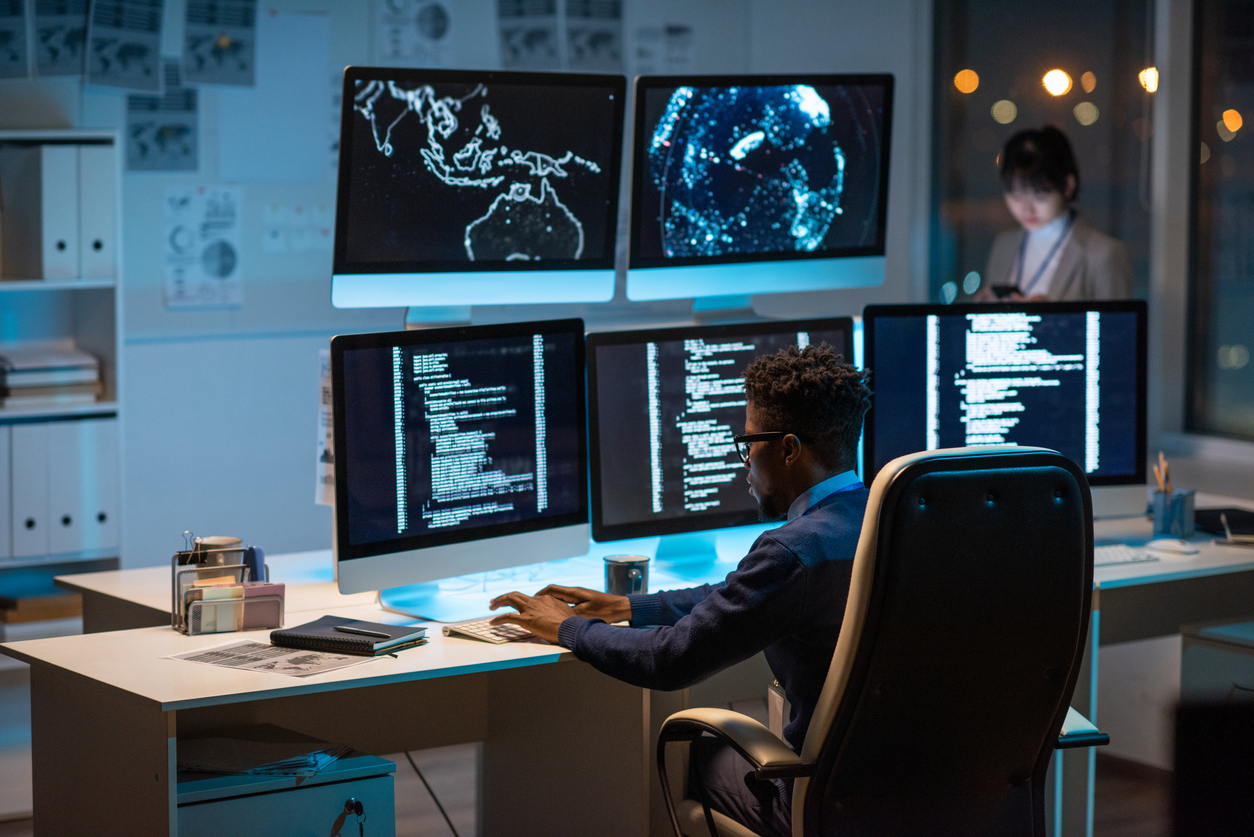 A cybersecurity expert works at a desk in front of a bank of monitors.