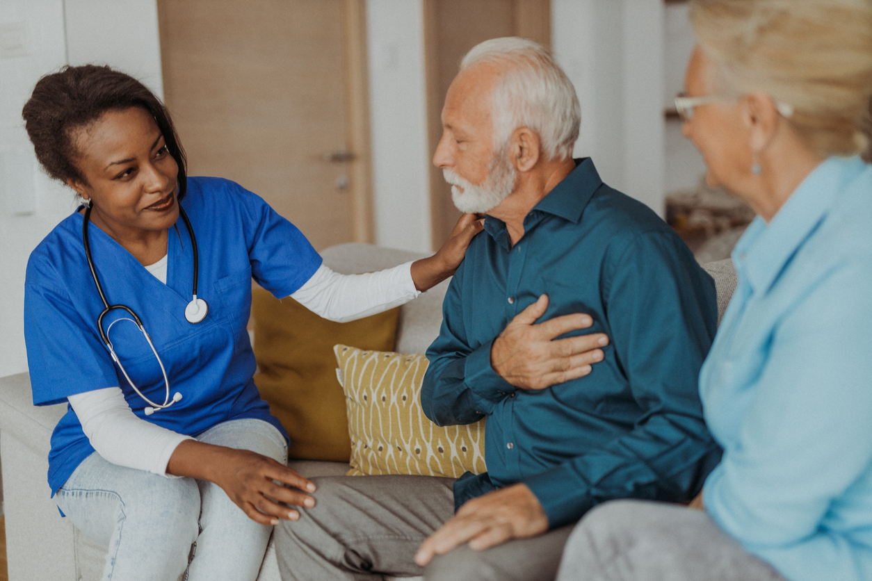 Nurse Sitting on a Couch With an Older Adult Patient and Another Adult.